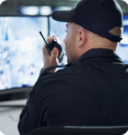 Security officer reviewing camera footage and talking on walkie-talkie, representing enhanced operations and compliance with Elevate workforce management.